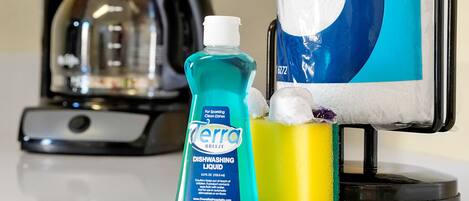 A bottle of Terra Breeze dishwashing liquid, a yellow sponge, and a coffee maker on a countertop.