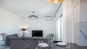 Un salon moderne avec un canapé gris, une table à manger dressée pour quatre personnes et un téléviseur à écran plat fixé au mur.