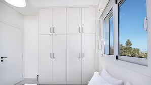Une chambre moderne avec une grande armoire, un lit avec du linge de lit blanc et une fenêtre donnant sur les arbres.