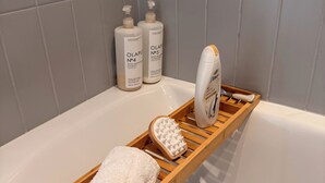 Une salle de bain avec un plateau en bois sur lequel sont posés une serviette et une brosse, et deux bouteilles de shampoing accrochées au mur.