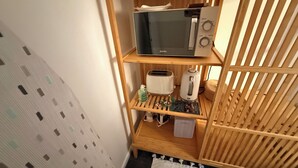 Une petite cuisine équipée d’un micro-ondes, d’un grille-pain et d’une petite étagère sur laquelle se trouvent une bouteille et un livre.