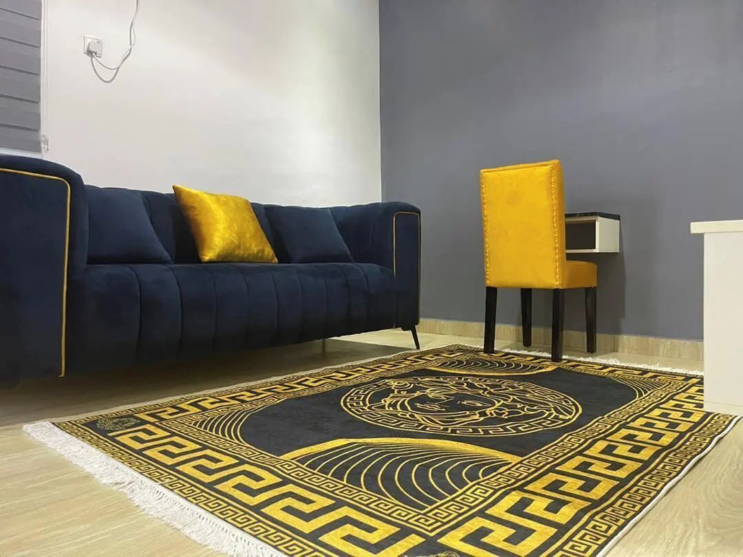 A room with a dark blue sofa, a yellow chair, and a patterned rug.