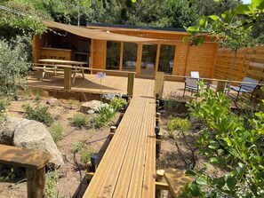 A wooden deck leading to a cabin with a dining area and outdoor seating. - Chalet l'elaegnus (Figari)