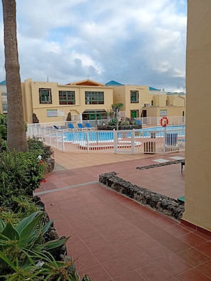 A pool area with a tiled deck, lounge chairs, and a lifebuoy. - Duplex Apartment, with private garden, in quiet complex (Calete de Fuste)