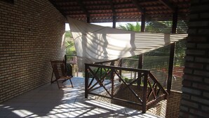Un patio coperto con pareti in mattoni, ringhiera in metallo e un tenda bianca che offre ombra.