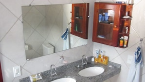 Un bagno con due lavabi, uno specchio, un mobiletto in legno con articoli da toilette e un asciugamano appeso al muro.