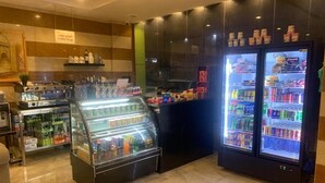 A coffee shop with a display case, a coffee machine, and a refrigerator stocked with beverages.