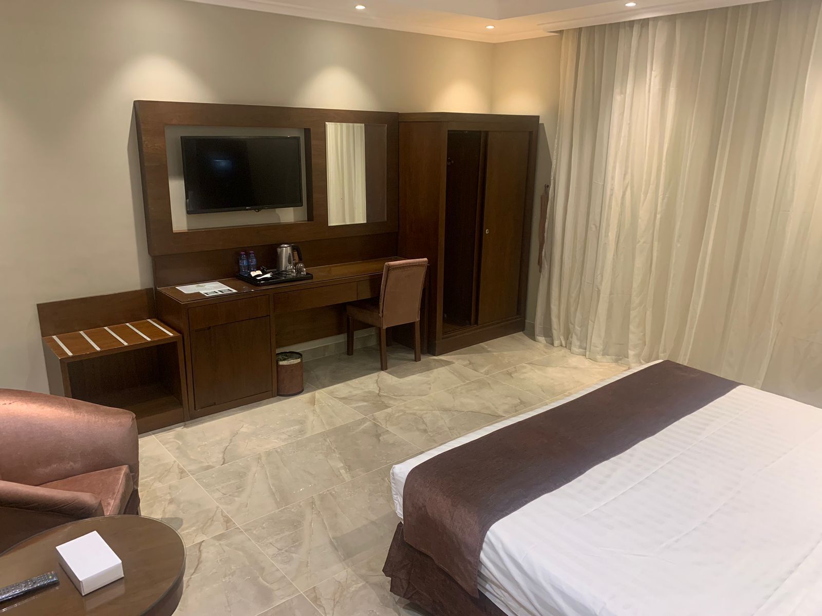 Quarto de hotel com uma cama, uma escrivaninha com cadeira, televisão e guarda-roupa.