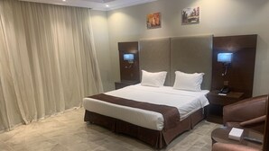 A hotel room with a large bed, a sitting area with a chair, a desk, and a television.