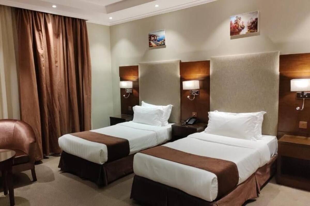 A hotel room with two beds, a sofa, a desk, and a large window with curtains.