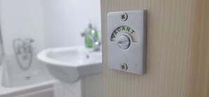 Un baño con un lavabo blanco e interruptor de luz en la pared que dice 'VACANT'.