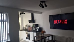 Cozinha moderna com forno embutido, máquina de café e torradeira. Uma televisão grande fixada na parede exibe o logotipo da Netflix.