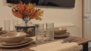 Mesa de jantar posta com tigelas, pratos, copos e um vaso com folhas de outono.