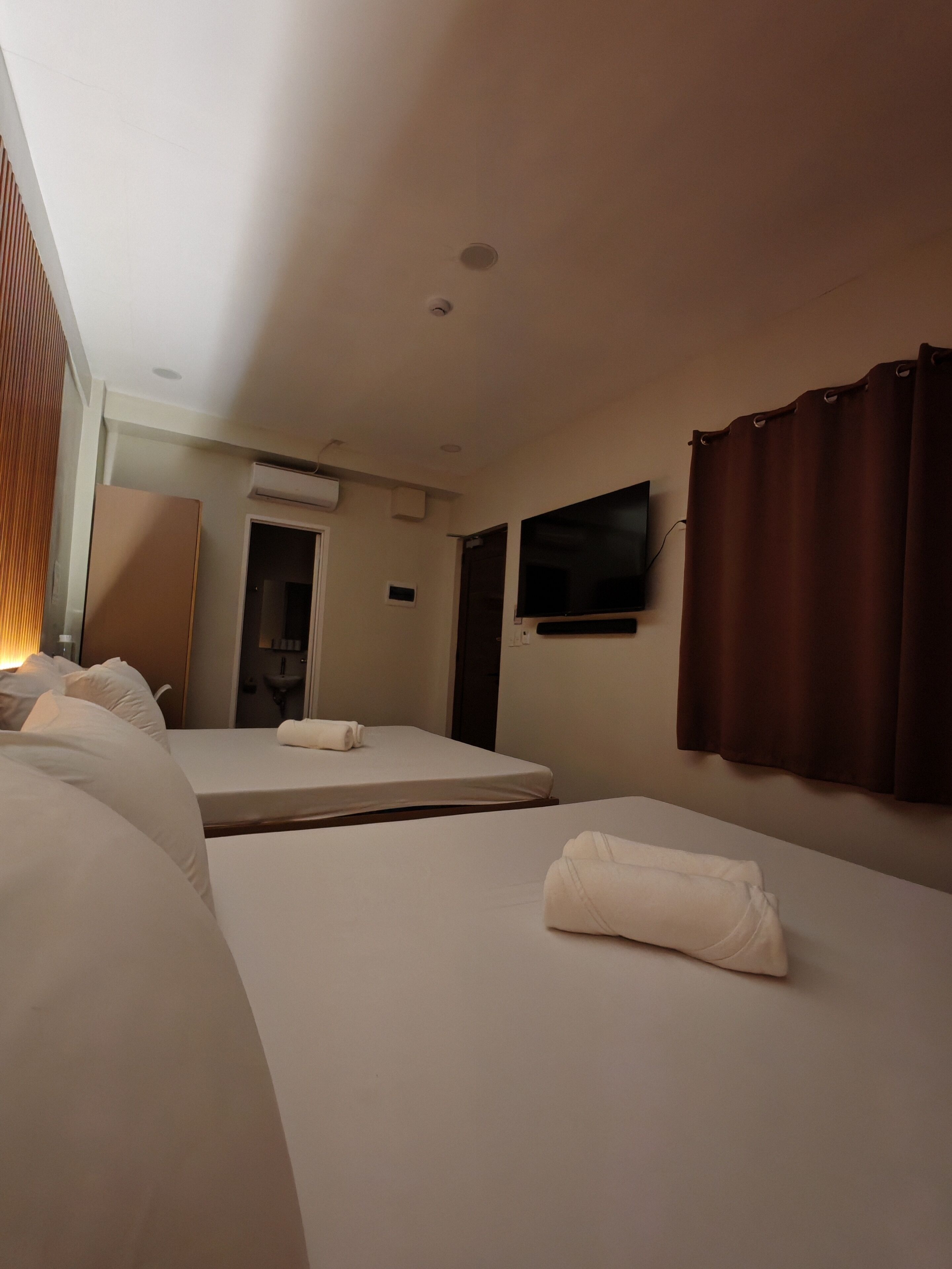 Une chambre d’hôtel avec deux lits, un téléviseur à écran plat, un appareil de climatisation et un rideau.