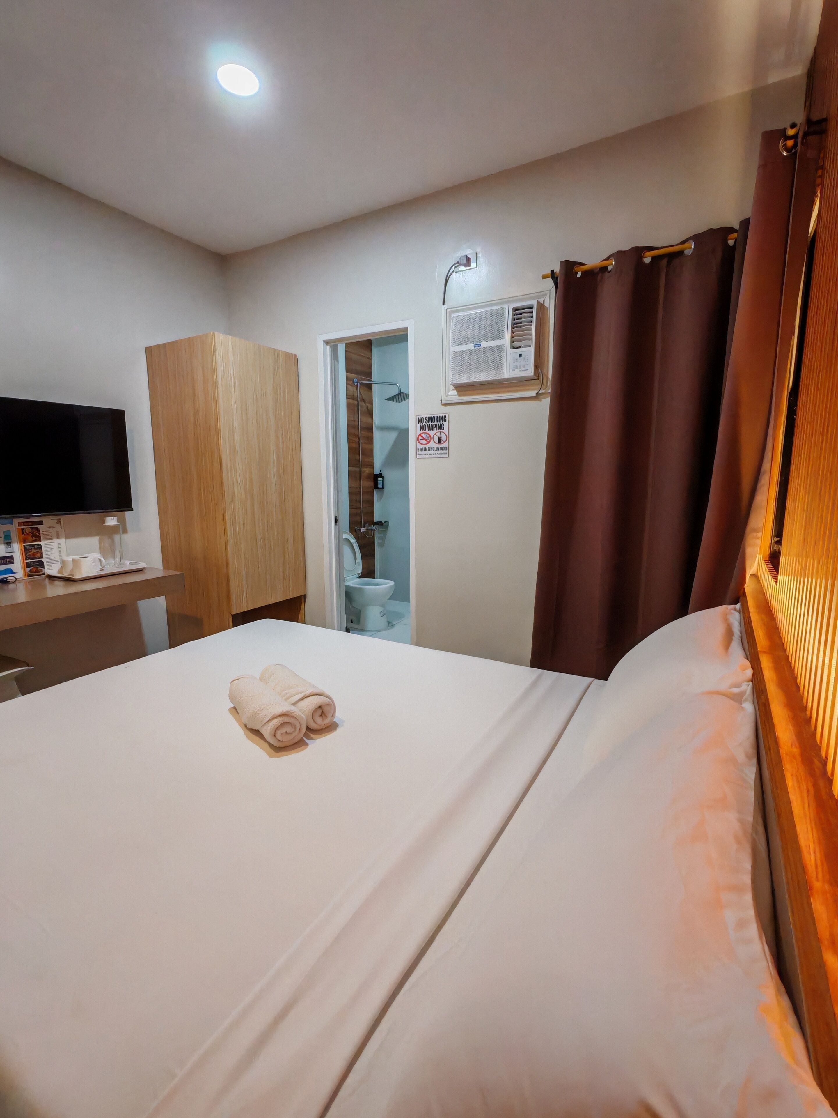 A hotel room with a bed, a desk, a television, a wardrobe, a bathroom, and a no smoking sign.