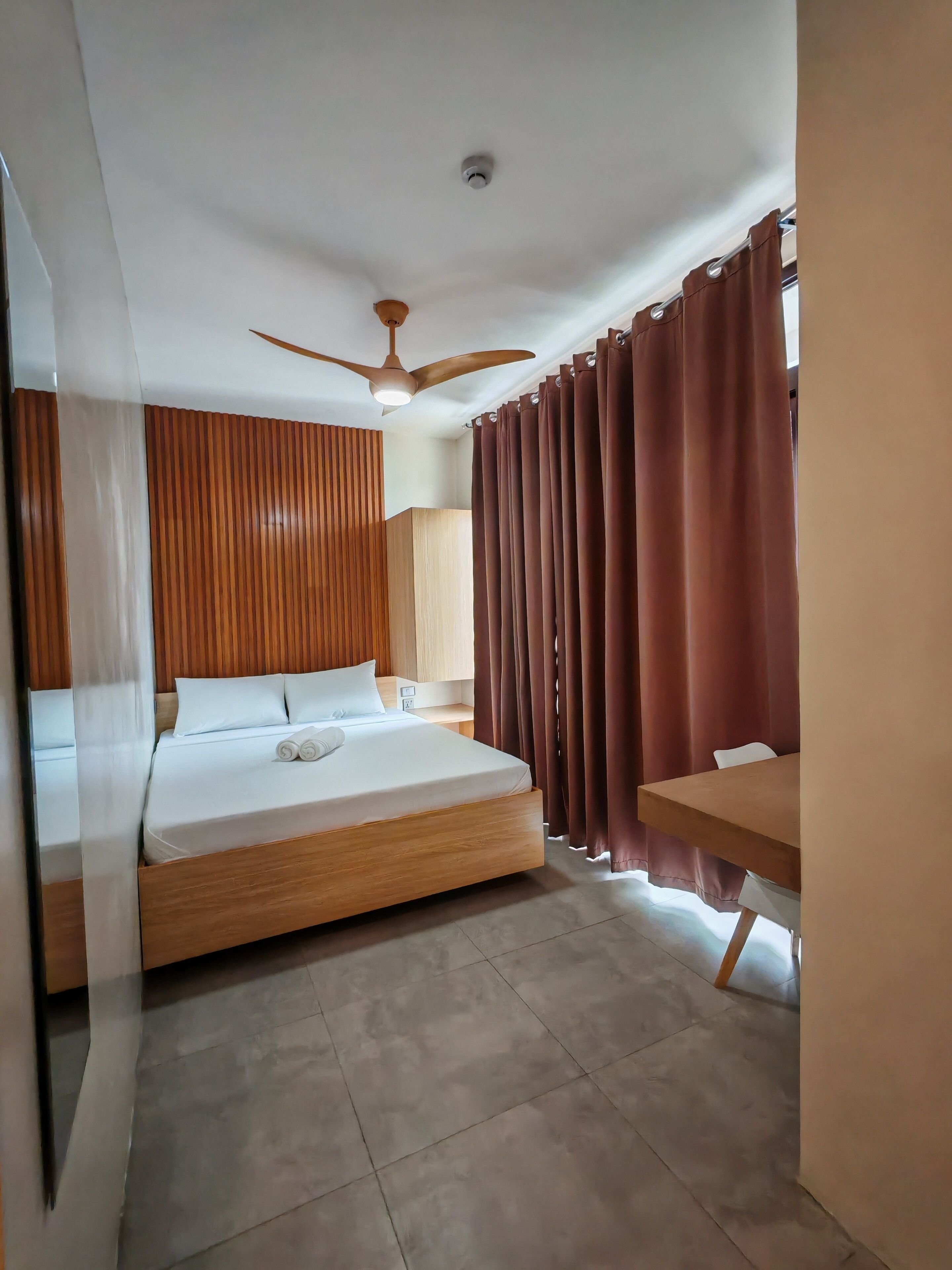 A modern bedroom with a wooden bed, a ceiling fan, and a view of a dining area.