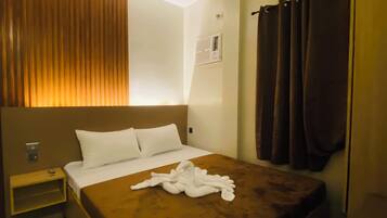 Habitación de hotel con una cama grande, una mesita de noche, aire acondicionado de pared y una ventana con cortinas.