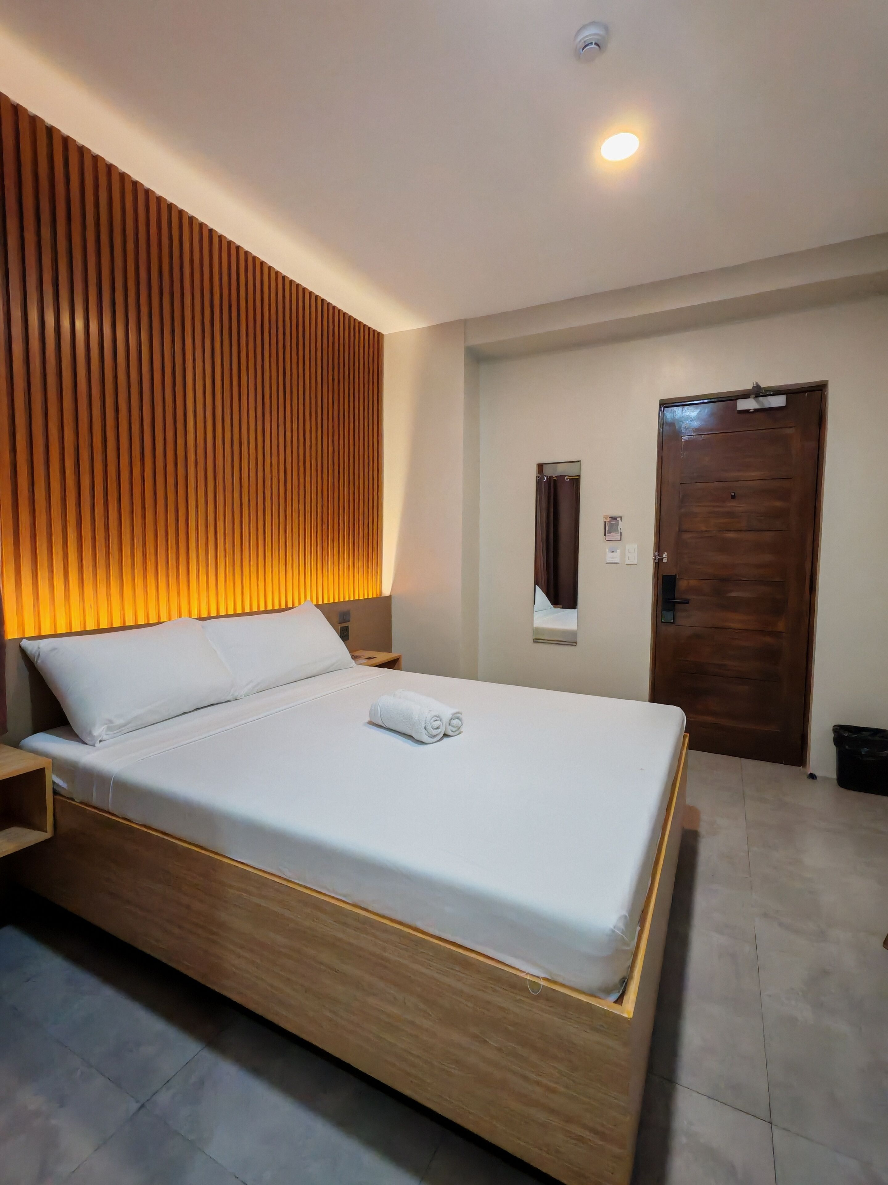 Habitación de hotel moderna con estructura de cama de madera, ropa de cama blanca y cabecera integrada con listones verticales.