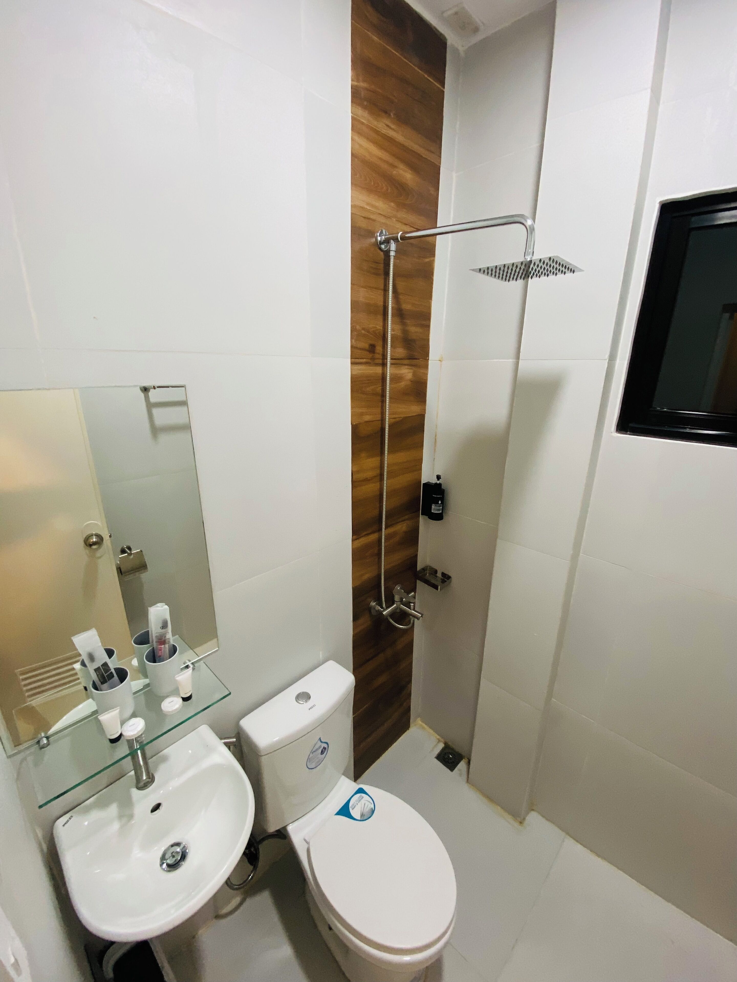 A modern bathroom with a glass sink, white toilet, and a shower with a wooden accent wall.