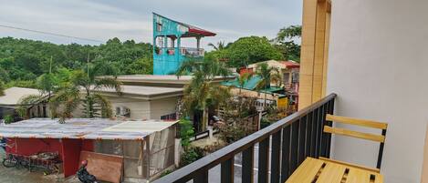 A balcony with a view of a blue building, a red structure, and a green area with trees.