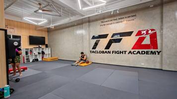 Un amplio espacio de entrenamiento con una frase motivadora en la pared, un saco de boxeo y una persona descansando.