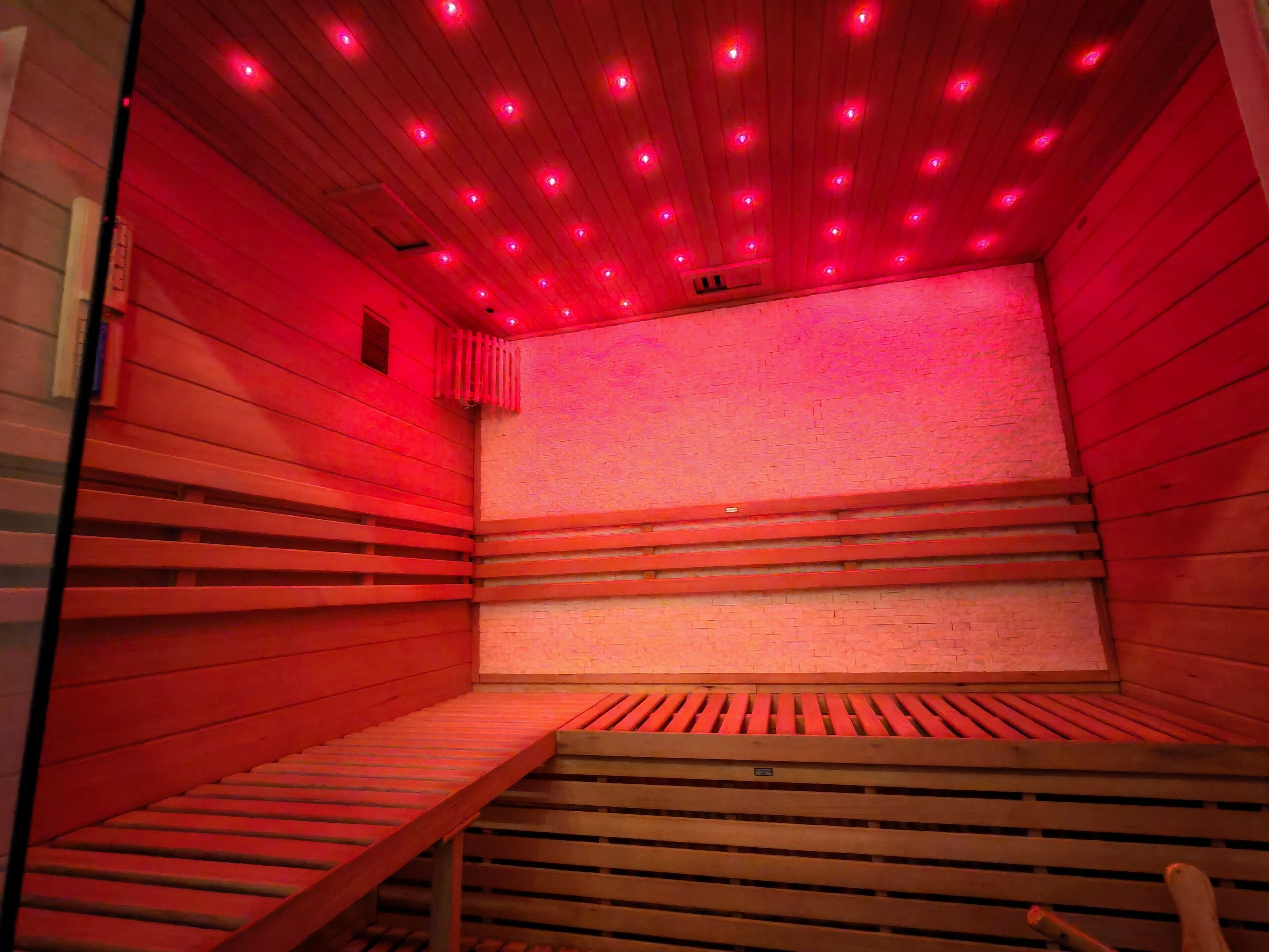 Una sauna con bancos de madera y techo inclinado con iluminación roja.