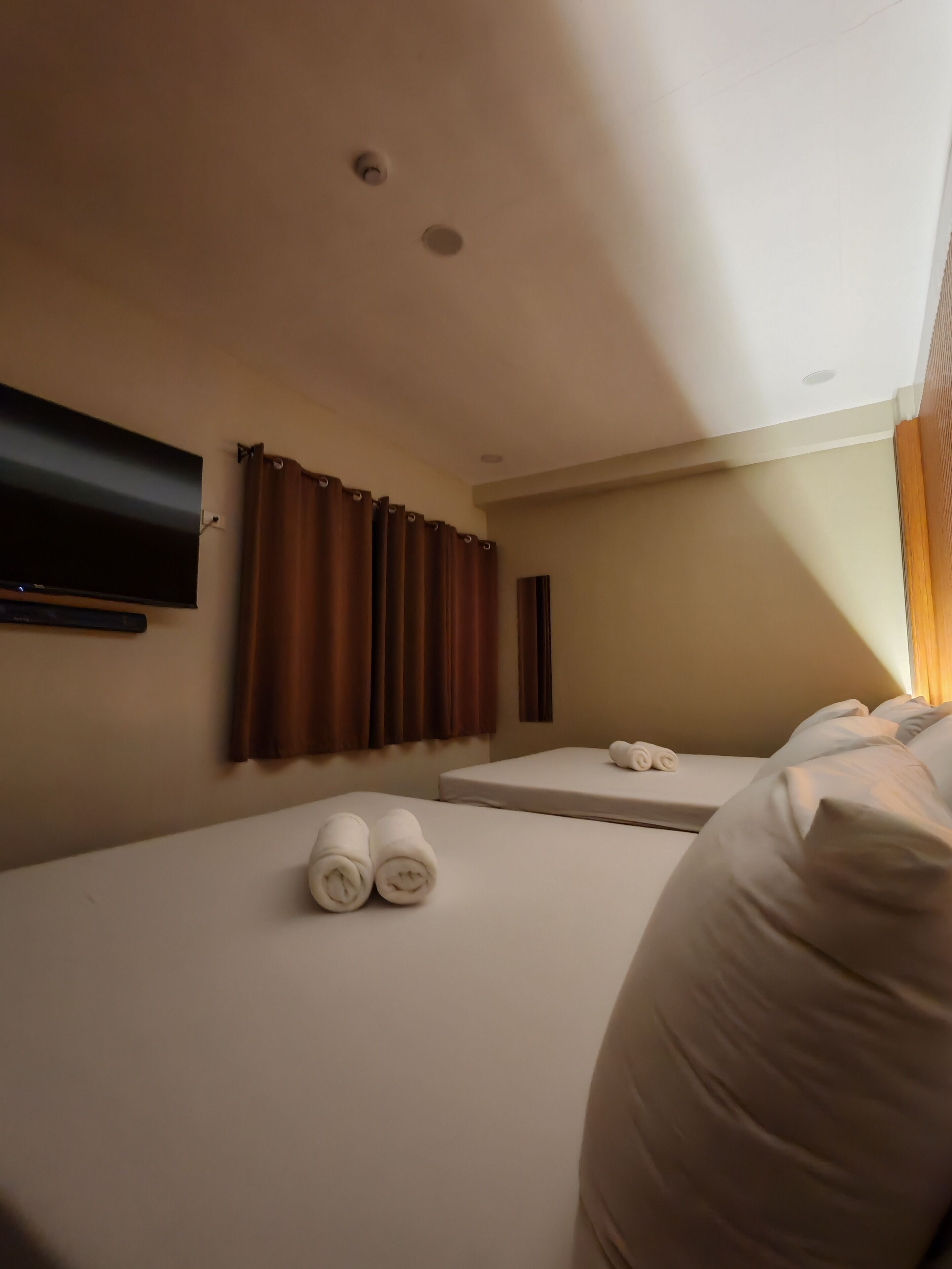 Une chambre d’hôtel avec deux lits, un téléviseur à écran plat fixé au mur et une fenêtre avec des rideaux.