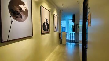 A hallway with framed artwork on the walls, a fire extinguisher, and a door at the end.