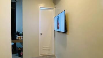 A narrow hallway with a white door, a mounted air conditioner, and a flat-screen TV on the wall.