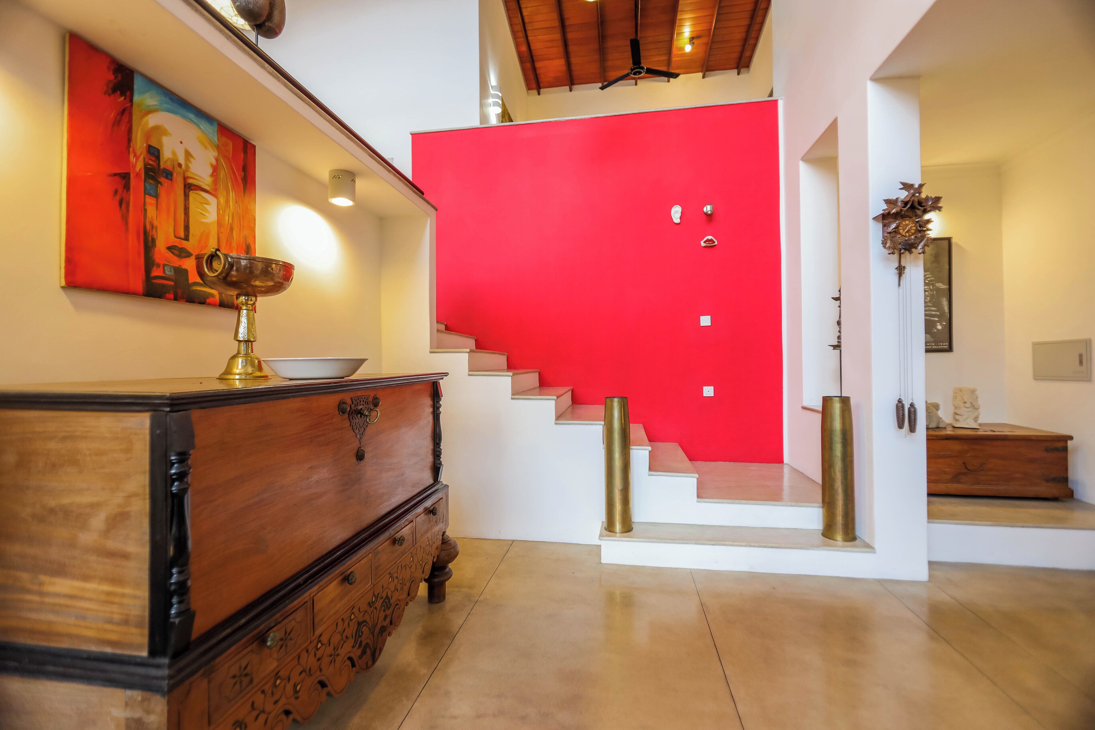 A staircase with a red wall, a wooden dresser with a brass bowl, and a ceiling fan.