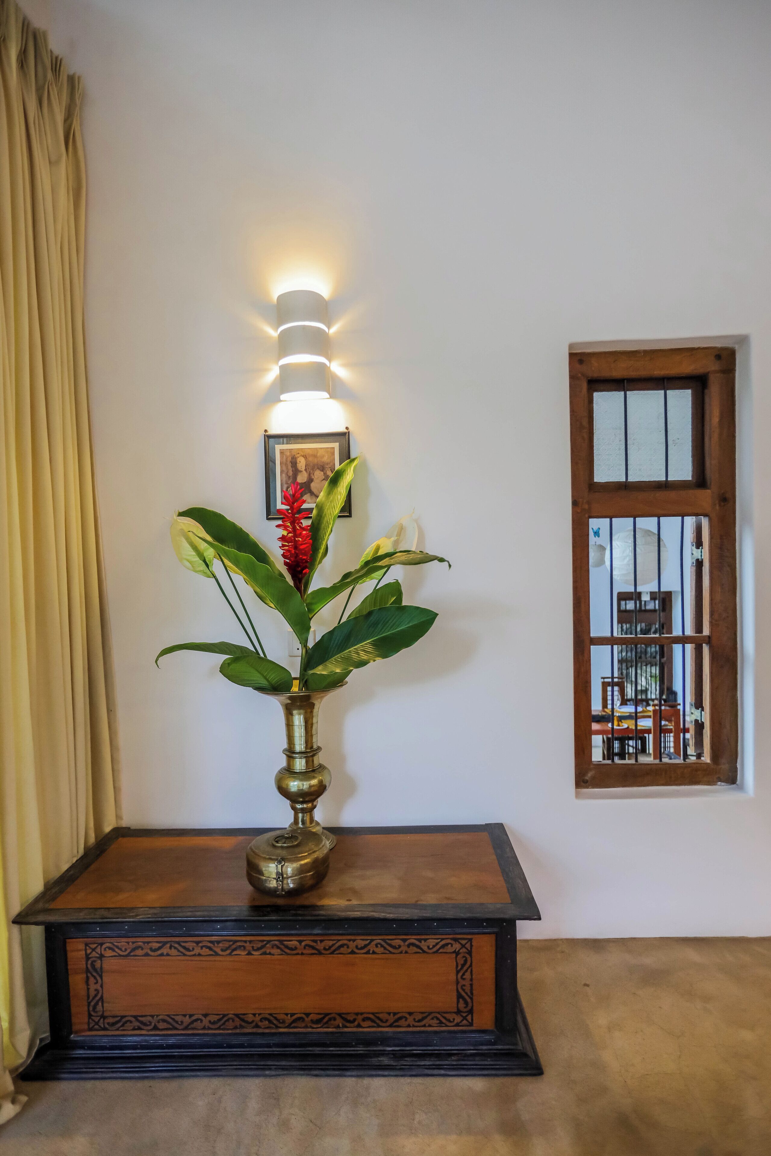 A table with a vase of plants and a wall-mounted light fixture.