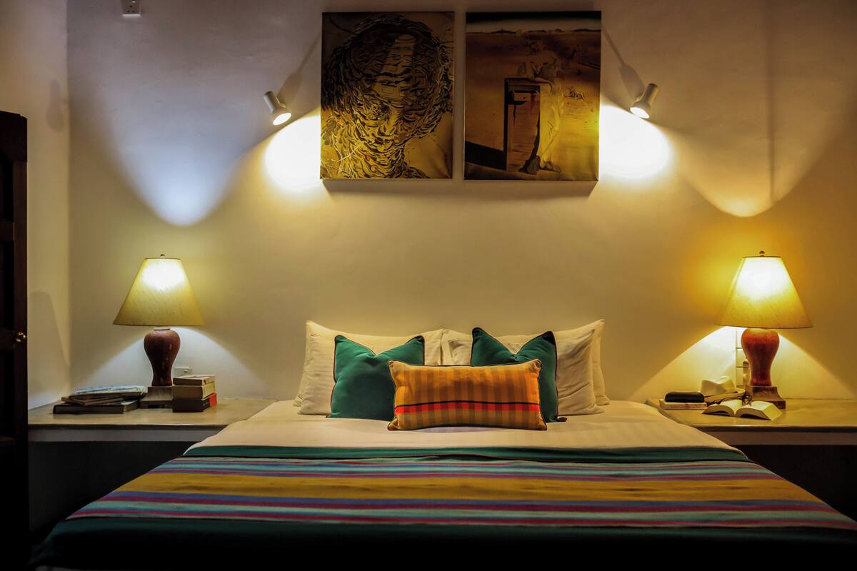 A neatly made bed with striped bedding, two bedside lamps, and a wall-mounted painting above it.