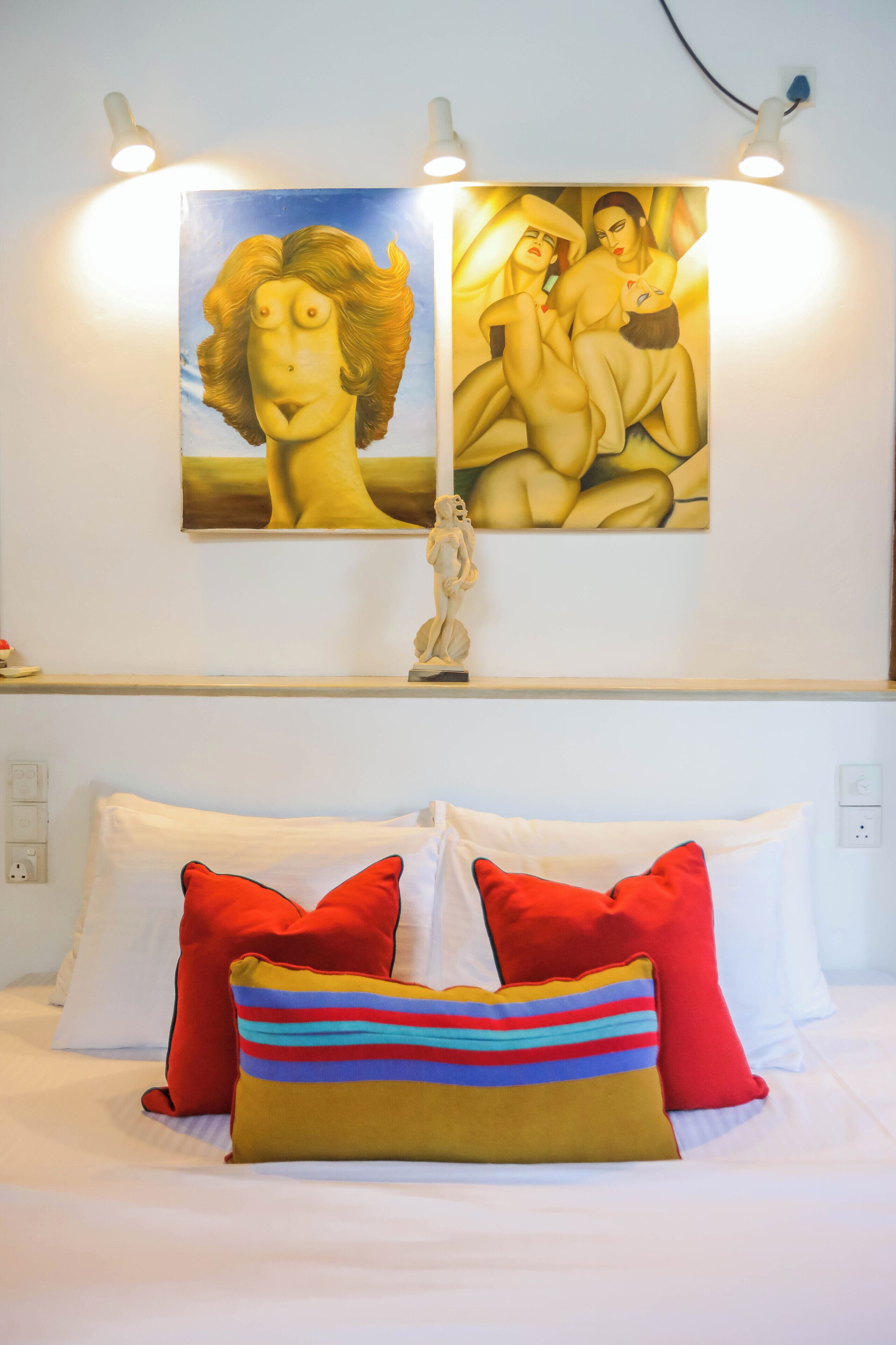 Une chambre d’hôtel avec un lit, des oreillers rouges et multicolores, et deux tableaux accrochés au mur.