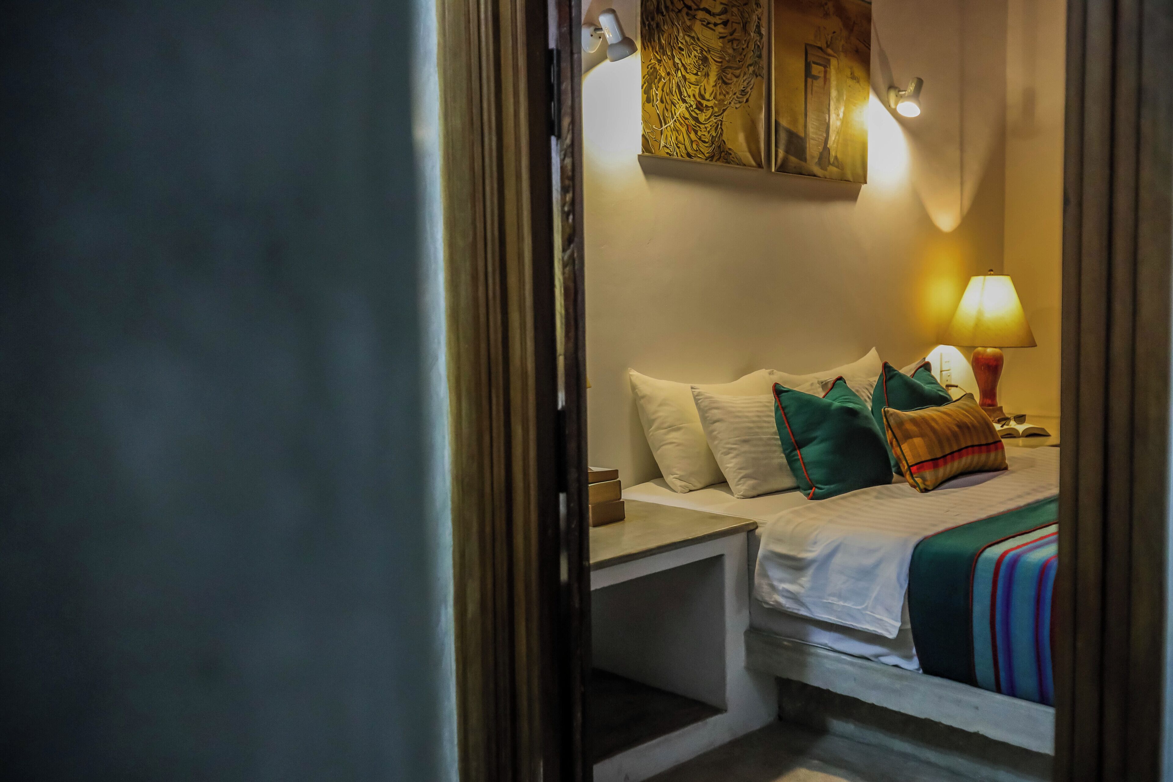 A hotel room with a bed, pillows, a nightstand, a lamp, and artwork on the wall.