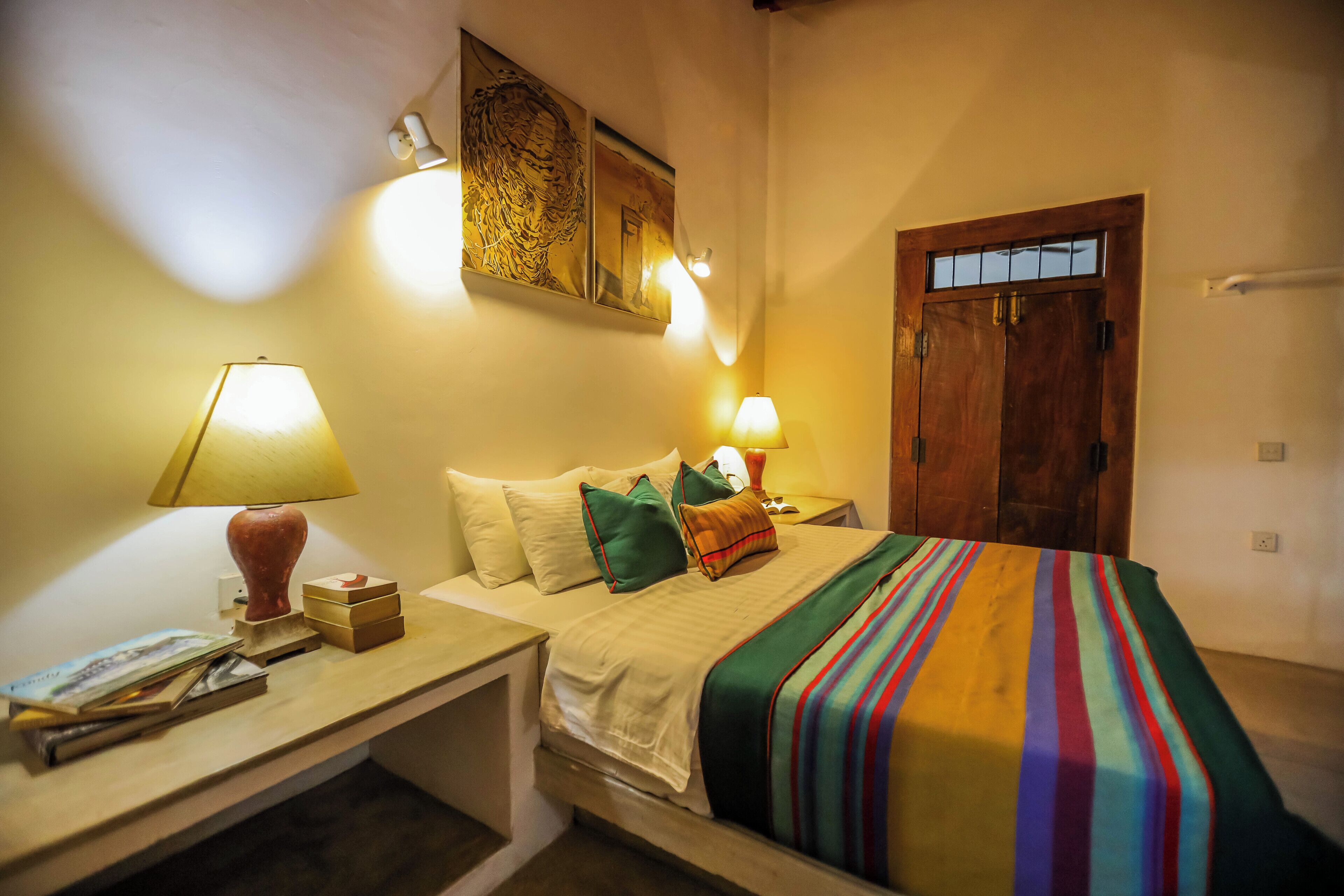 Quarto de hotel bem arrumado com cama, luminárias de cabeceira, mesa de cabeceira e um quadro na parede.