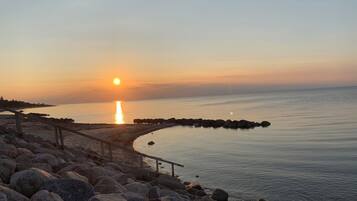 Et kystlandskab med solnedgang over vandet, en klippefyldt kystlinje og en træpromenade.