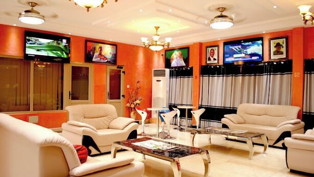 A hotel lobby with a modern design, featuring leather sofas, a central coffee table, and a television mounted on the wall. - Fams Embassy Suites (Badagry)