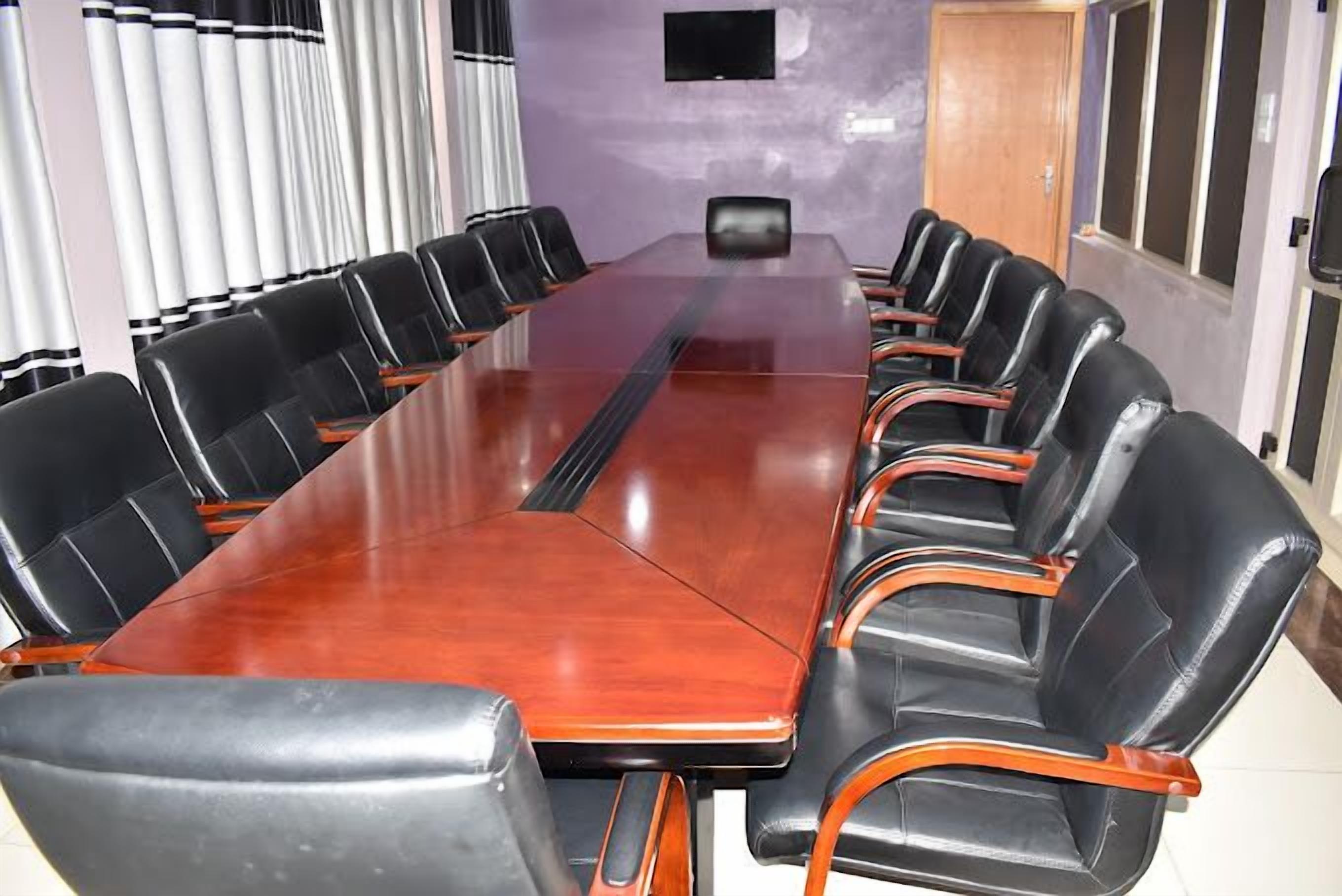 A conference room with a long table and black leather chairs with wooden armrests.