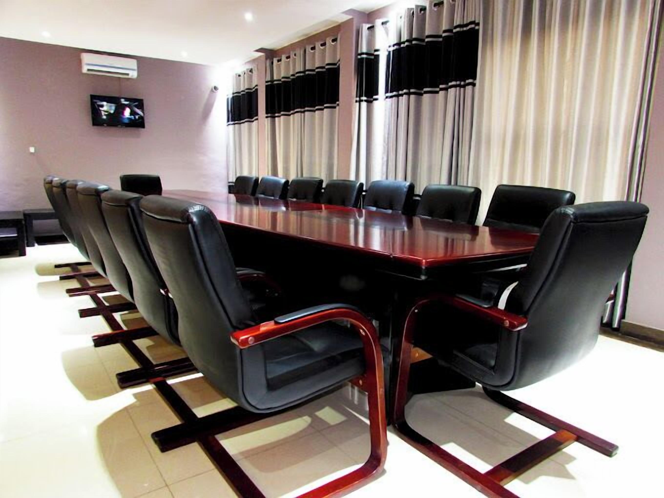 A conference room with a long table, black leather chairs, a flat-screen TV, and a large window with curtains.