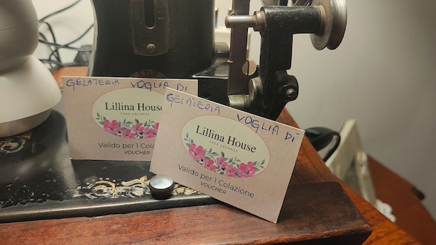 Eine alte Nähmaschine mit dekorativem Emblem, ein Holztisch und zwei Visitenkarten für 'Lillina House' mit floralem Muster.