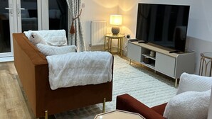 Una sala de estar moderna con un sofá, una mesita, un televisor y una lámpara.