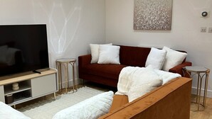 Una sala de estar moderna con un televisor de pantalla plana grande, un sofá marrón, cojines blancos y una mesita auxiliar.