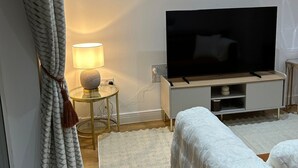 Un dormitorio moderno con una televisión de pantalla plana, una mesita de noche con lámpara, un sofá y un ventanal con cortinas.