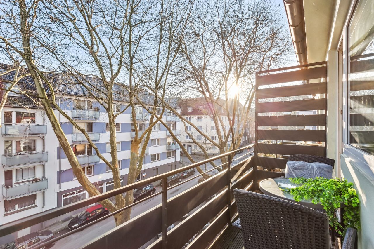 A balcony with wicker furniture, a potted plant, and a view of residential buildings.