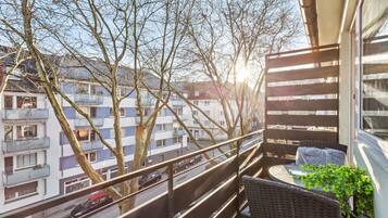 A balcony with wicker furniture, a potted plant, and a view of residential buildings.