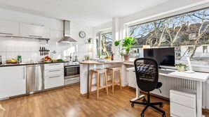 Une cuisine moderne avec des meubles blancs, un plan de travail en bois et une grande fenêtre donnant sur un quartier résidentiel.