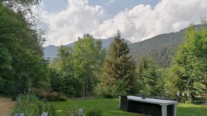 Un jardín con un banco y plantas en macetas, rodeado de árboles y montañas.