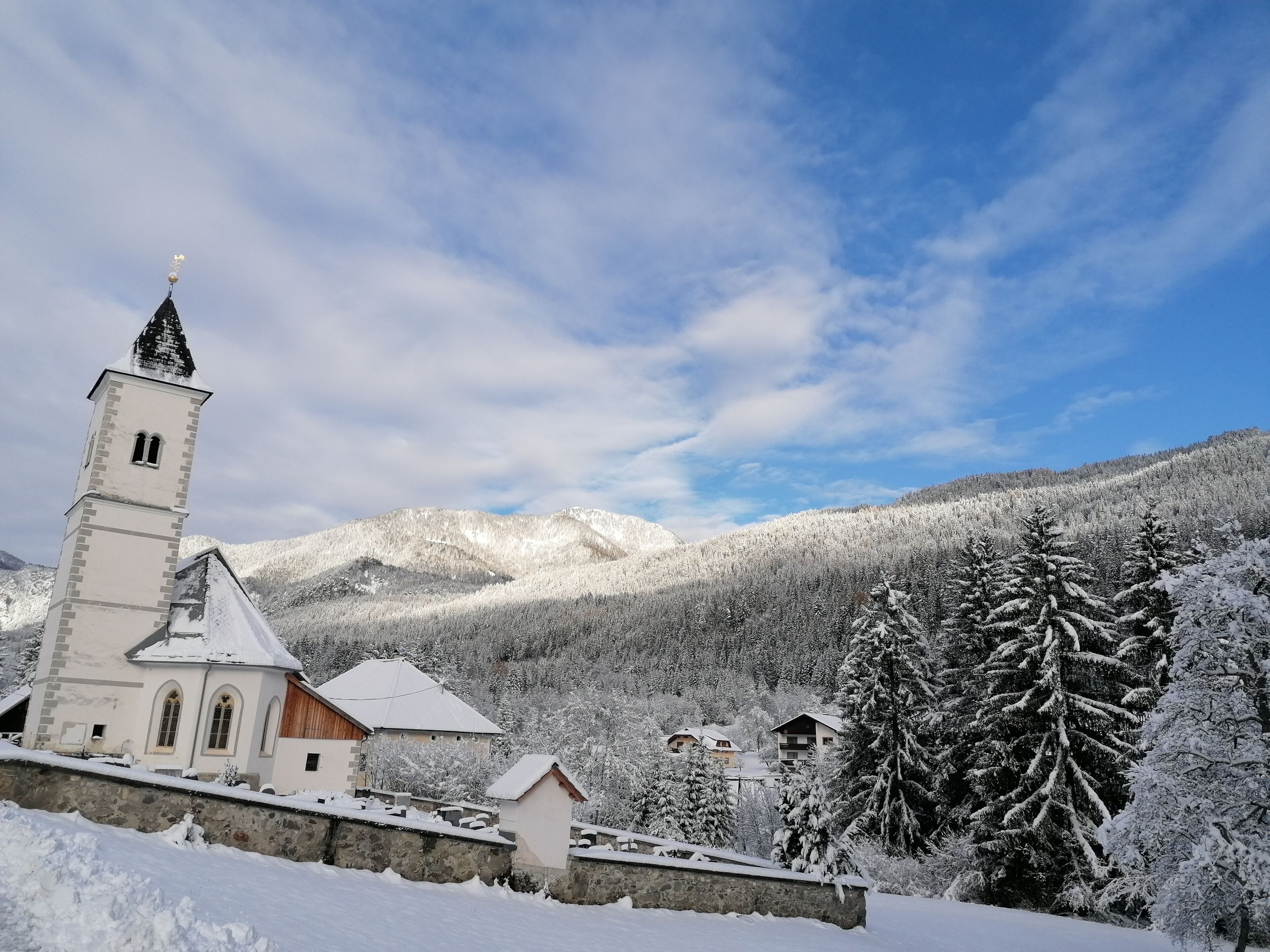 A church with a bell tower, surrounded by snow-covered trees and mountains.
