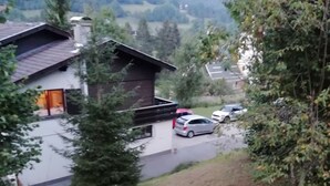 Un barrio residencial con una casa de techo inclinado, un garaje visible y una entrada con coches estacionados.