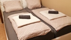 Una cama doble con ropa de cama y almohadas estampadas, suelo de madera y pared color crema.
